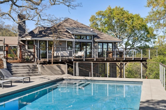 rear view of house with stairway, a wooden deck, a chimney, an outdoor pool, and a patio