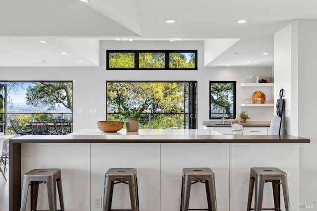 kitchen with modern cabinets, a breakfast bar, open shelves, white cabinetry, and recessed lighting