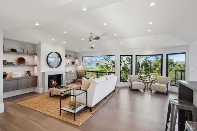 living area featuring a glass covered fireplace, recessed lighting, lofted ceiling, and wood finished floors