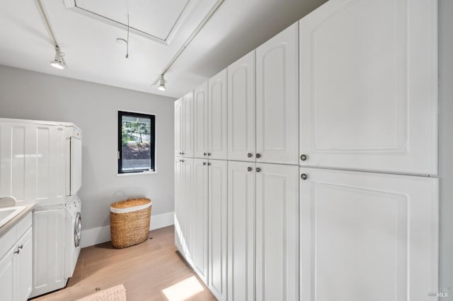 laundry area with baseboards, light wood finished floors, attic access, cabinet space, and stacked washer and dryer