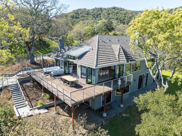 back of property with a tile roof, a chimney, and a view of trees