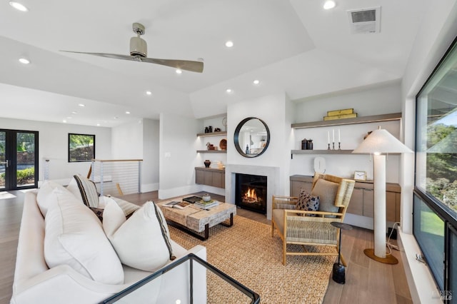 living room featuring visible vents, recessed lighting, a warm lit fireplace, wood finished floors, and a ceiling fan