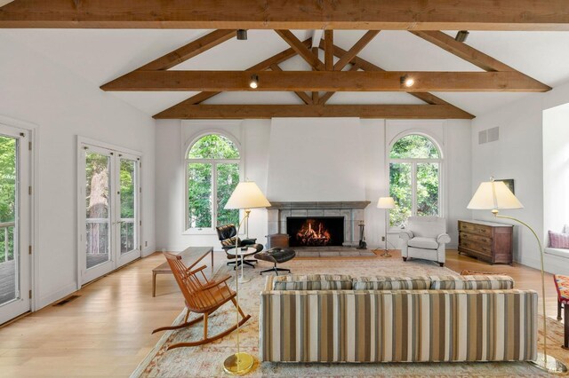 living room featuring beam ceiling, visible vents, light wood-style floors, and a lit fireplace