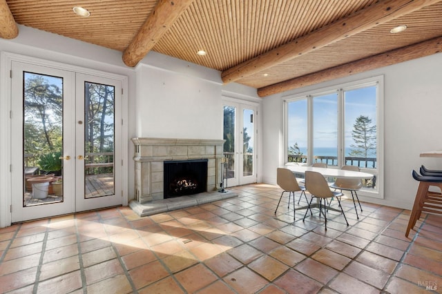 unfurnished dining area with beam ceiling, recessed lighting, french doors, a tiled fireplace, and wooden ceiling