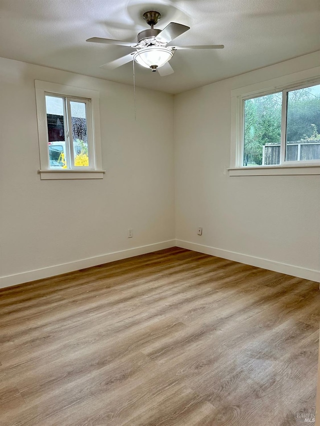 spare room with light wood-style flooring, a textured ceiling, baseboards, and a ceiling fan