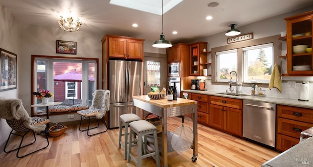 kitchen with tasteful backsplash, light wood finished floors, brown cabinets, stainless steel appliances, and a sink