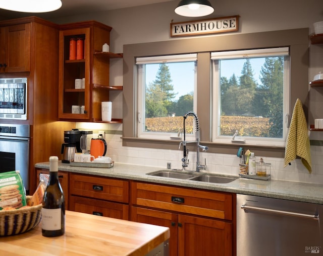 kitchen featuring tasteful backsplash, a sink, brown cabinetry, stainless steel appliances, and open shelves