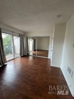 empty room with baseboards, wood finished floors, visible vents, and a textured ceiling