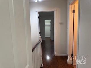 corridor with baseboards, an upstairs landing, and dark wood-style flooring