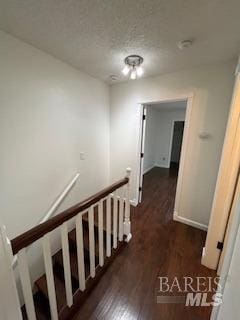 corridor with an upstairs landing, a textured ceiling, baseboards, and wood finished floors