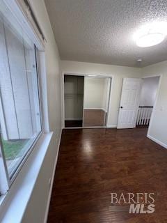 unfurnished bedroom featuring a closet, a textured ceiling, baseboards, and wood finished floors
