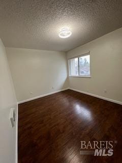 spare room featuring baseboards, a textured ceiling, and dark wood-style flooring