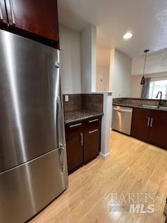 kitchen with a sink, dark countertops, light wood finished floors, and stainless steel appliances