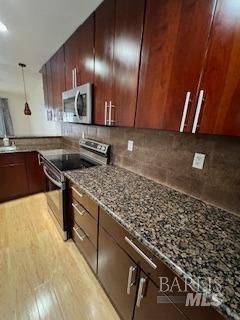 kitchen with pendant lighting, light wood-style flooring, light stone counters, backsplash, and stainless steel appliances