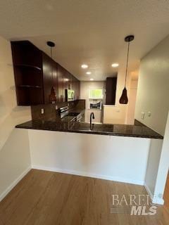 kitchen featuring dark countertops, pendant lighting, a peninsula, and wood finished floors