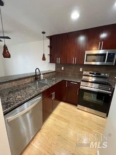 kitchen featuring light wood-style flooring, appliances with stainless steel finishes, a peninsula, and a sink