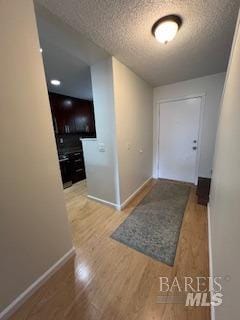 hallway featuring wood finished floors, baseboards, and a textured ceiling
