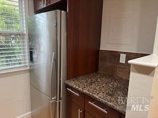 kitchen featuring decorative backsplash, light stone counters, and stainless steel fridge