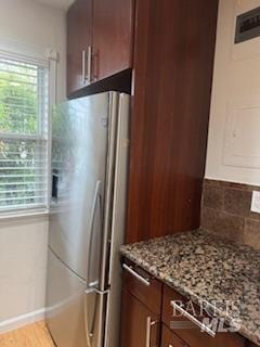 kitchen with light stone counters, baseboards, light wood-style flooring, freestanding refrigerator, and tasteful backsplash