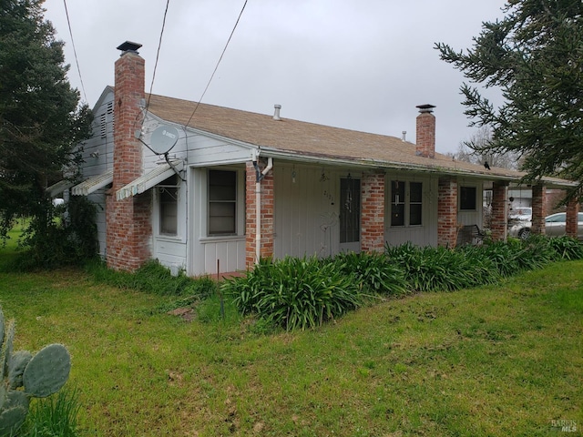 rear view of property featuring brick siding, a chimney, and a yard