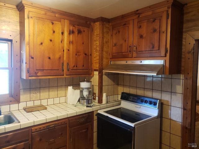 kitchen with backsplash, electric stove, brown cabinetry, and under cabinet range hood