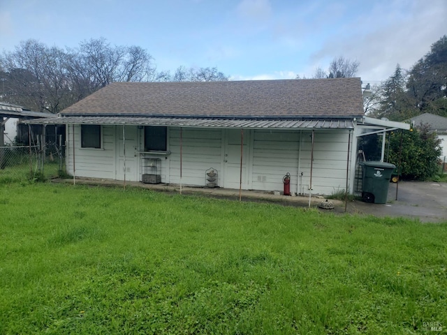 rear view of property featuring a carport, a lawn, roof with shingles, and fence