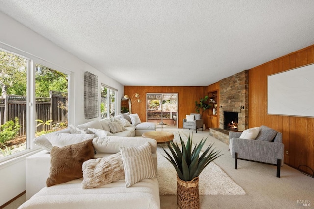 living room with a stone fireplace, wooden walls, carpet flooring, and a textured ceiling