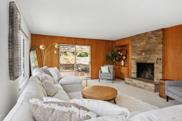 living area featuring built in features, a textured ceiling, wooden walls, a stone fireplace, and carpet flooring