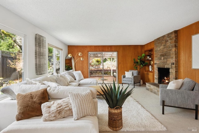 living room featuring light colored carpet, a stone fireplace, wooden walls, and a textured ceiling