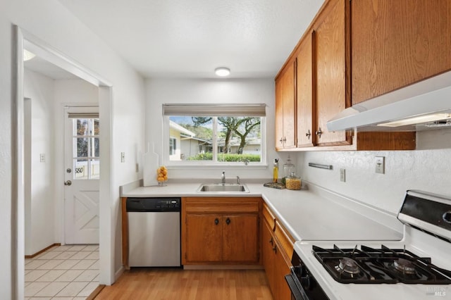 kitchen featuring range with gas stovetop, a sink, light countertops, stainless steel dishwasher, and brown cabinets