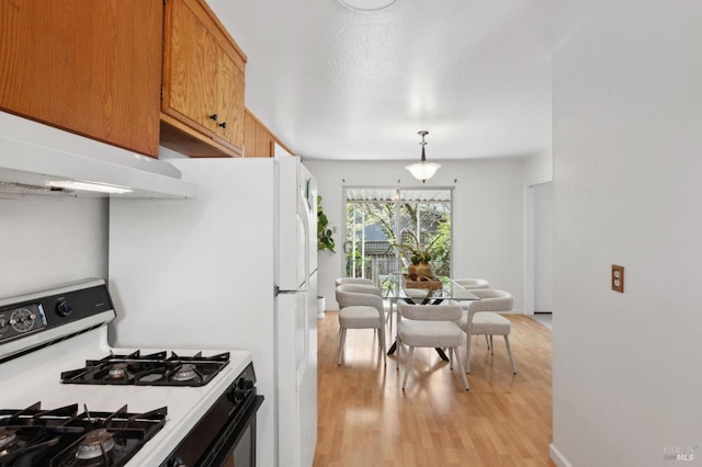 kitchen featuring under cabinet range hood, decorative light fixtures, range with gas stovetop, light wood-style floors, and brown cabinetry