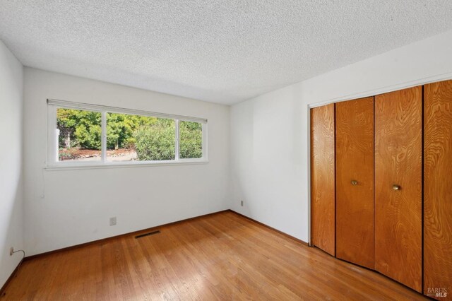 unfurnished bedroom with light wood-style flooring, visible vents, a closet, and a textured ceiling