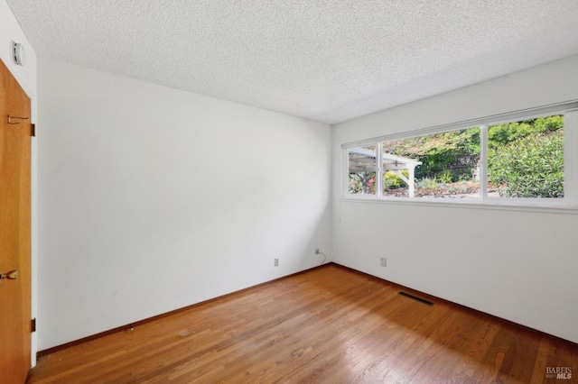 spare room with baseboards, wood finished floors, visible vents, and a textured ceiling