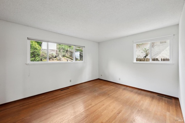 spare room featuring visible vents, light wood-style flooring, and a textured ceiling