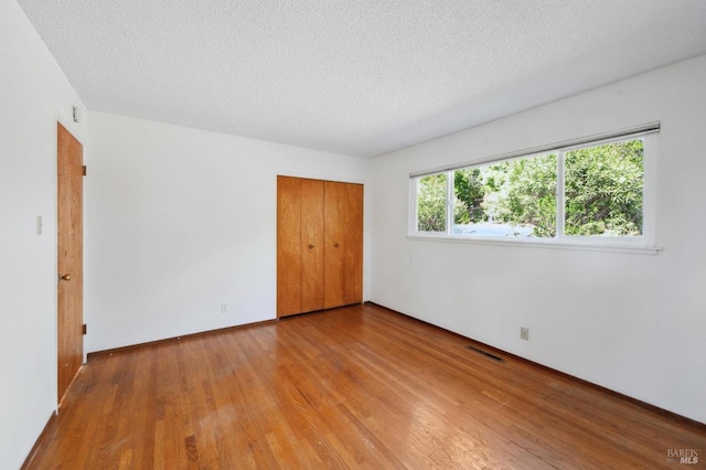 unfurnished bedroom featuring baseboards, a closet, a textured ceiling, visible vents, and wood finished floors