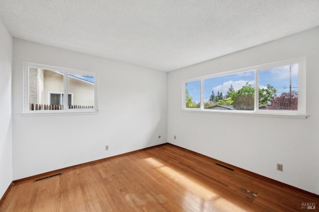 unfurnished room with visible vents, a textured ceiling, and wood finished floors