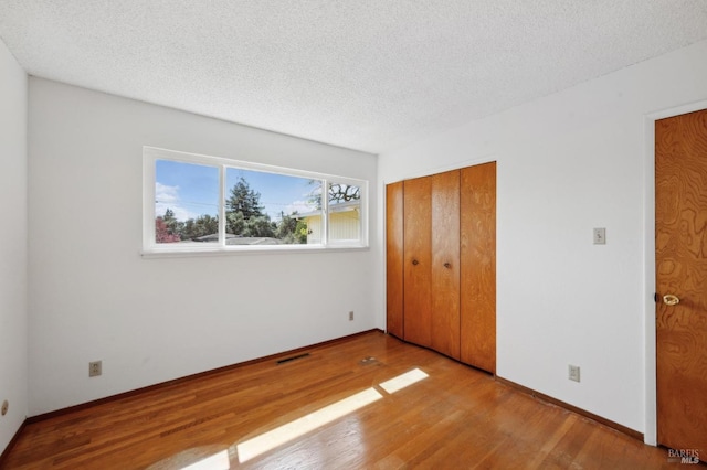 unfurnished bedroom with visible vents, baseboards, a textured ceiling, and wood finished floors