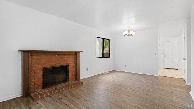 unfurnished living room with baseboards, a notable chandelier, wood finished floors, and a fireplace