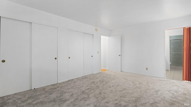 unfurnished bedroom with connected bathroom, two closets, and carpet