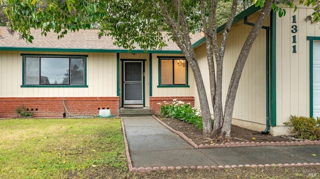 view of exterior entry with a lawn and brick siding