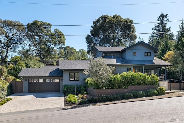 view of front of property with board and batten siding, driveway, a garage, and fence