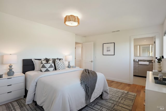 bedroom featuring connected bathroom, light wood-style floors, visible vents, and baseboards