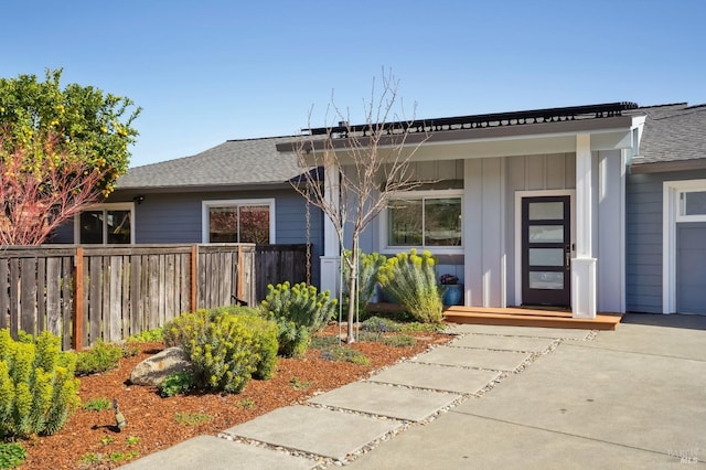 view of front of home featuring board and batten siding, a shingled roof, concrete driveway, and fence