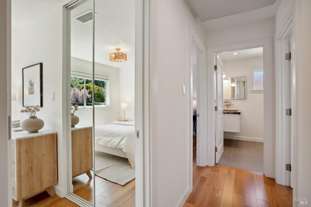 hallway with light wood-type flooring, baseboards, and visible vents