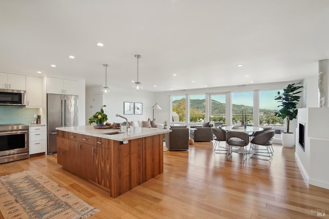 kitchen with backsplash, open floor plan, light wood-style flooring, stainless steel appliances, and a sink