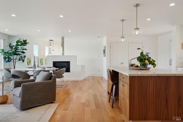 living area with a glass covered fireplace, recessed lighting, light wood-type flooring, and baseboards