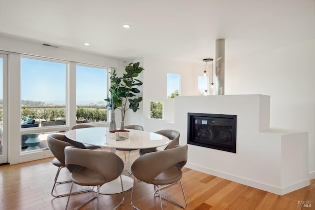 dining area featuring light wood finished floors, a glass covered fireplace, recessed lighting, and visible vents