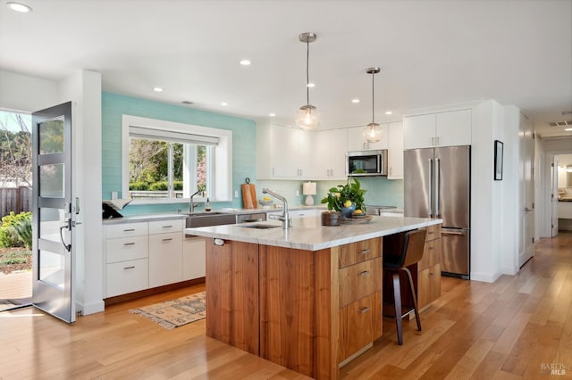 kitchen with a kitchen island with sink, a sink, stainless steel appliances, light wood-style floors, and backsplash