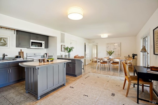 kitchen with visible vents, a breakfast bar, a kitchen island, white appliances, and light countertops