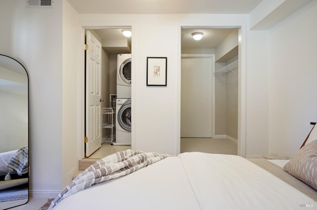 bedroom featuring a spacious closet, baseboards, stacked washer and clothes dryer, and a closet